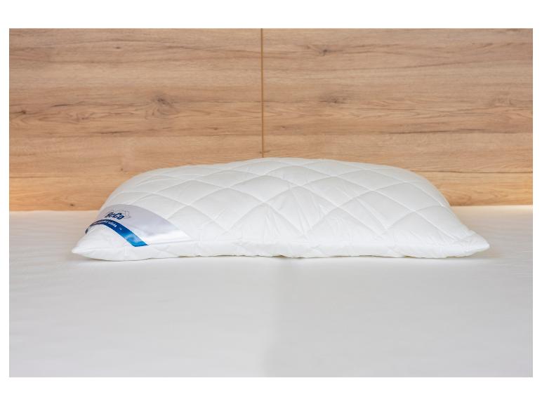 Wit gewatteerd kussen op een bed met een houten hoofdbord.