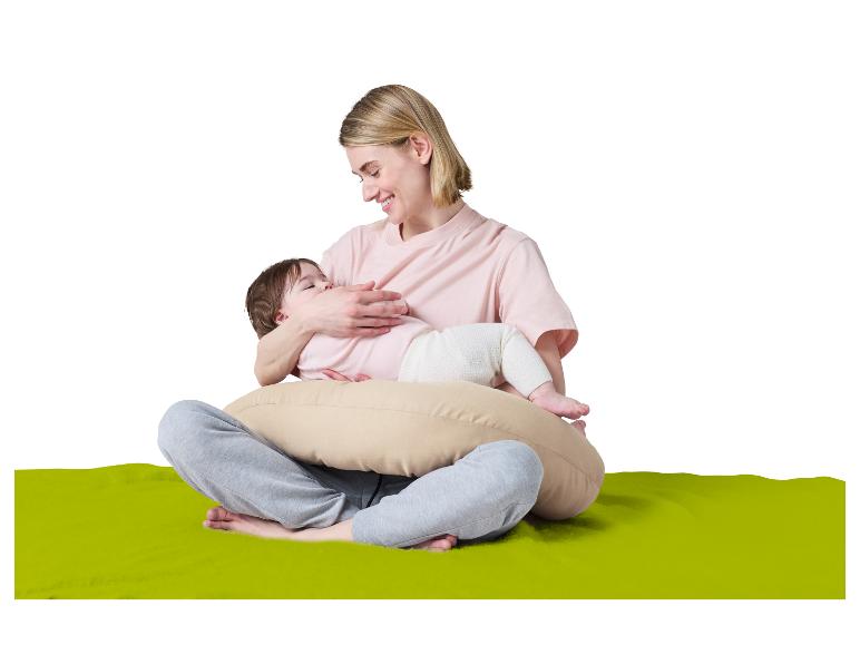 Lachende moeder die haar baby borstvoeding geeft op een voedingskussen, zittend op een groene mat.