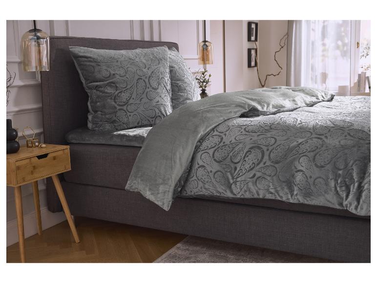 Een bed met grijs beddengoed met paisley-patroon en een houten nachtkastje.
