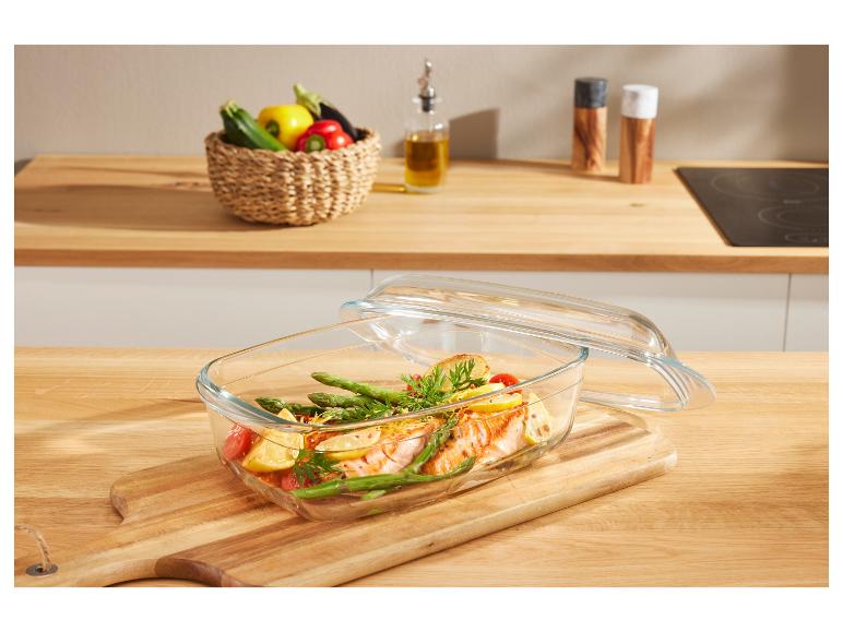 Glazen ovenschaal met gebakken zalm en asperges op een houten snijplank.