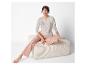 Vrouw in een beige pyjama met de tekst 'Sleep Dream Relax' zit op een lichte poef.