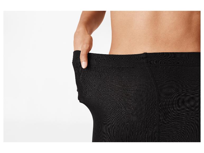 Een persoon trekt de tailleband van een zwarte legging uit elkaar om te laten zien dat deze te groot is.