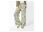 Damesbroek met bloemenprint, groen overhemd en witte sneakers.