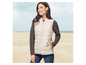 Een vrouw draagt een beige gewatteerde vest op het strand.