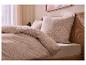 Beige beddengoed met paisley patroon en kussens op een bed met houten hoofdeinde.