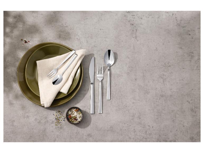 Roestvrijstalen bestekset, borden en kruiden op een grijze achtergrond.