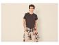 Man in donker T-shirt met 'Resilience'-opdruk, beige broek en geruit overhemd om de taille geknoopt.