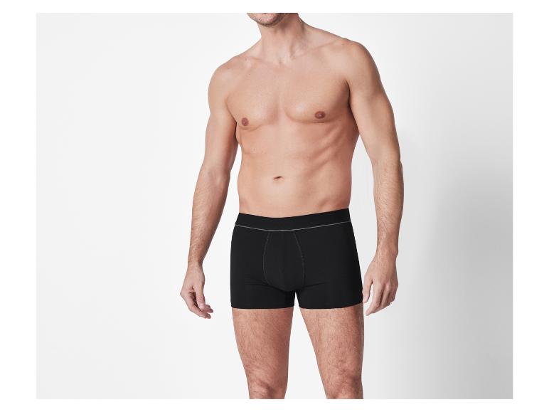 Man zonder shirt in zwarte boxershorts tegen een witte achtergrond.