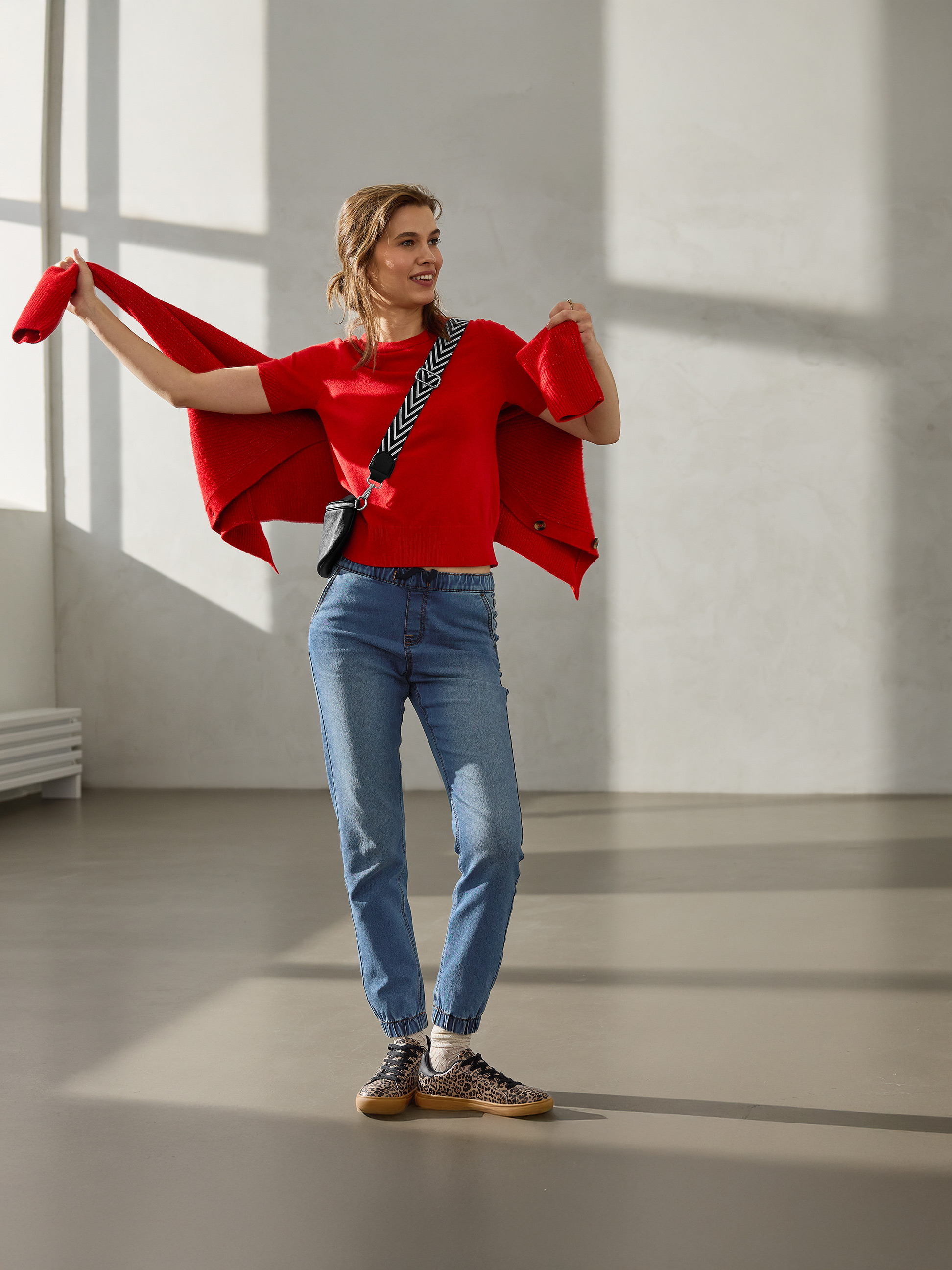 Vrouw in rode trui, rood vest, jeans en sneakers met luipaardprint.