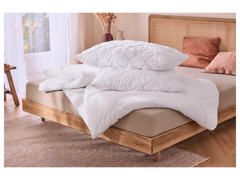 Witte doorgestikte kussens en dekbed op een bed met houten frame en rotan hoofdeinde.