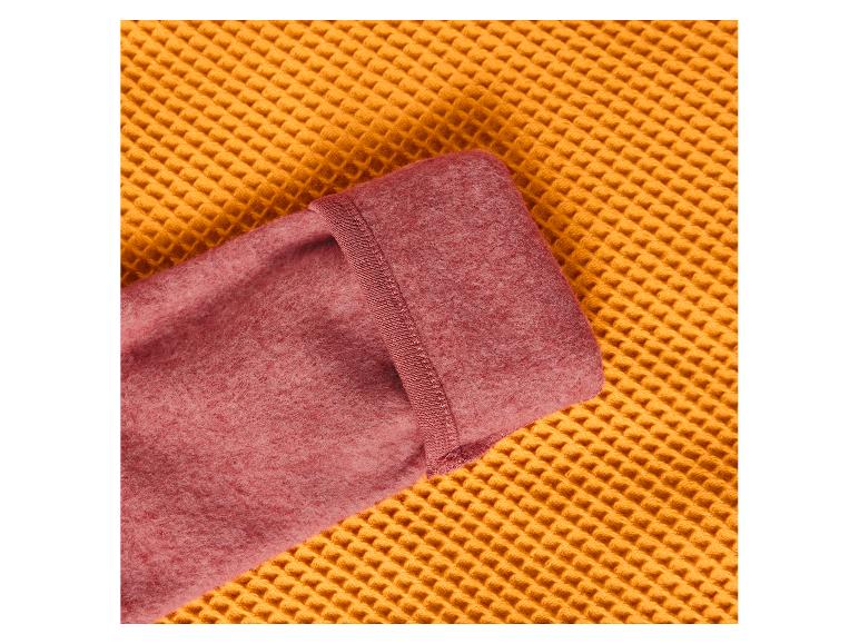 Close-up van een gevouwen roze fleecedeken op een geel wafelgeweven oppervlak.