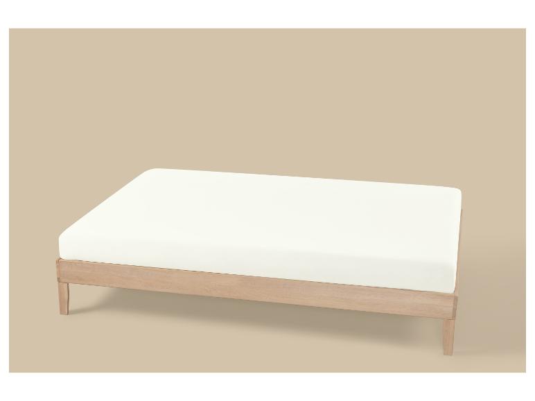 Licht houten bedframe met wit matras op beige achtergrond.