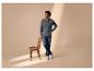 Man in jeans en shirt met lange mouwen staat naast een houten stoel.
