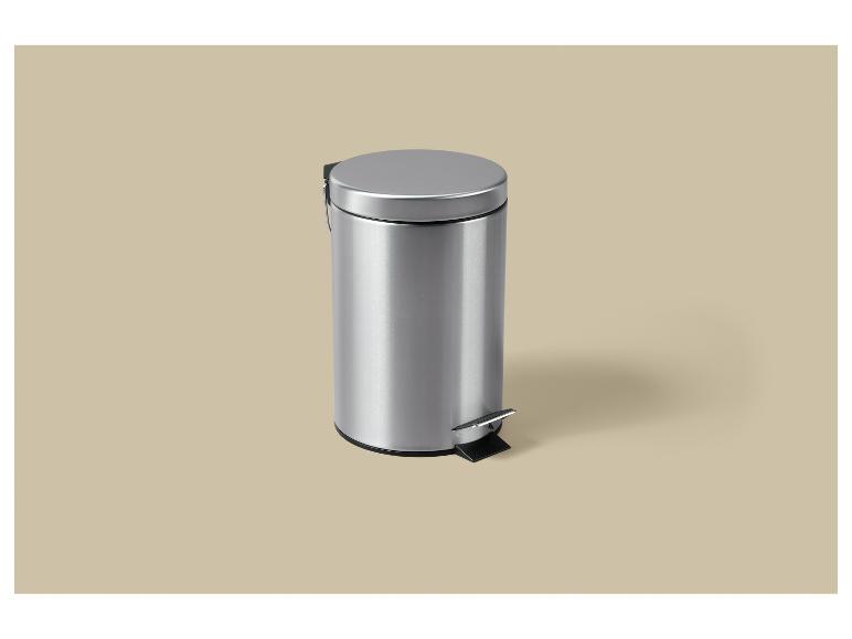 Een zilveren pedaalemmer met deksel op een beige achtergrond.