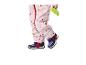 Kind in roze regenpak met hartjesprint en donkerblauwe schoenen, met een groen speeltje in de hand.