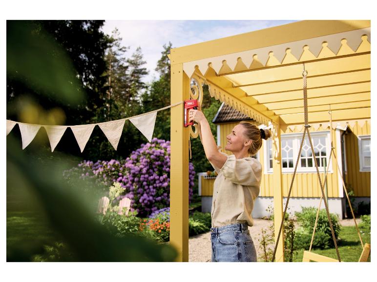 Vrouw bevestigt vlaggetjes met LIVARNO® Handtacker »R53 T&F« aan een gele pergola.