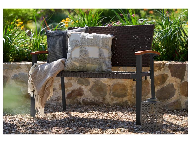 Tuinbank met kussens en plaid, tegen een achtergrond van groen en een stenen muur.