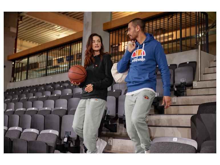Twee personen dragen grijze Ellesse joggingbroeken in een sportstadion.