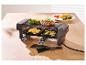 Raclette grill met biefstuk, broccoli en groenten, plus twee spatels op een houten tafel.