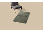 Grijze stoel en groen vloerkleed met abstract rozenpatroon op beige achtergrond.