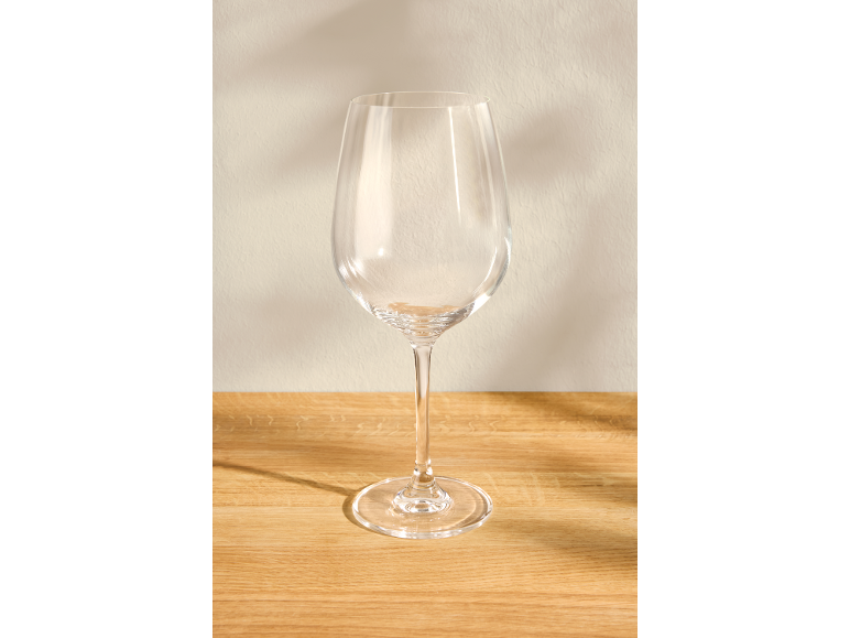 Leeg wijnglas op een lichte houten tafel met een beige achtergrond.