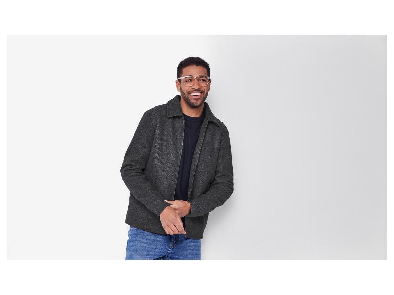 Lachende man met bril, draagt een grijze jas en jeans.