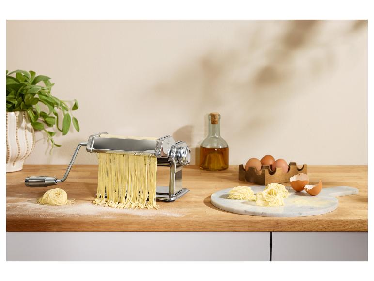 Pastamachine met verse pasta, eieren en olijfolie op een houten aanrecht.