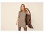 Vrouw in beige gebreide jurk met bruine jas over haar schouder.