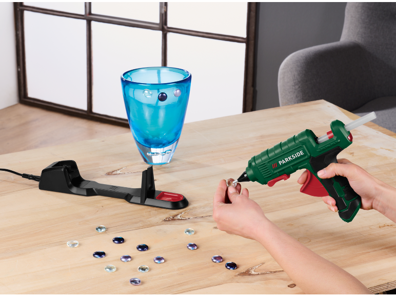 Heteluchtpistool versiert een glazen vaas met edelstenen op een houten tafel.