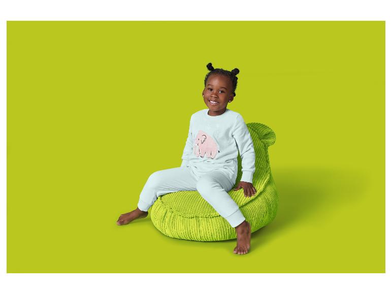 Een lachend meisje zit op een groene zitzak, gekleed in een lichte pyjama met een roze olifant.