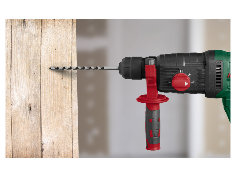 Een groene boormachine met een rode handgreep boort een gat in een houten plank.