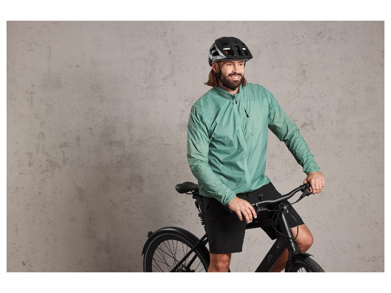 Een man met een helm en een jas rijdt op een zwarte fiets.