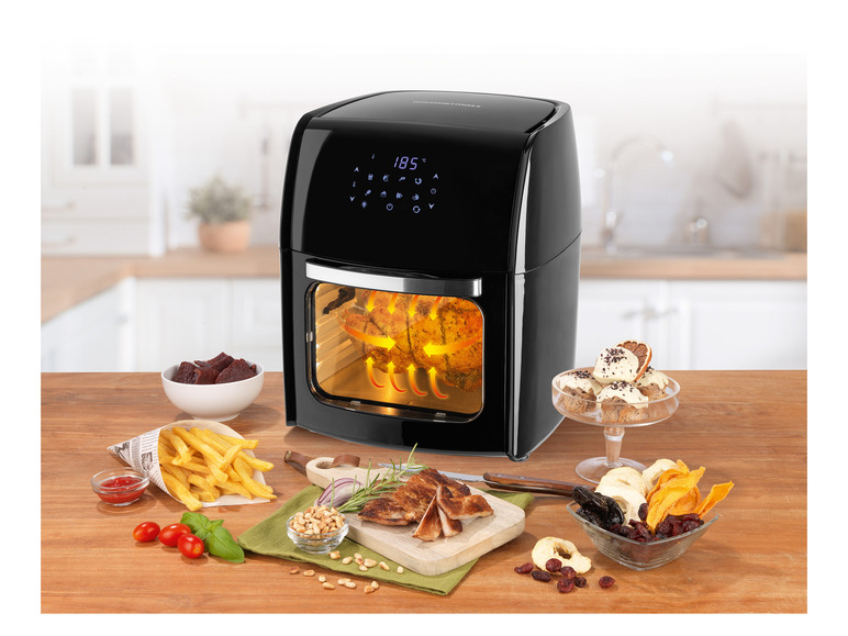 Een zwarte Gourmetmaxx airfryer met een gebraden kip erin, omringd door gefrituurde frietjes, snacks en gedroogd fruit.