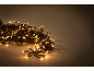 Kerstverlichting met warmwitte LED-lampjes en groene dennentakken op een lichte achtergrond.