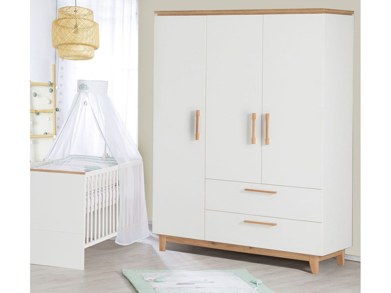 Een witte babywieg met een hemel en een witte kledingkast met houten details.