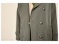 Groene trenchcoat met schildpadknopen en een beige overhemd eronder.