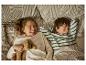 Twee lachende kinderen in bed, één met een teddybeer.