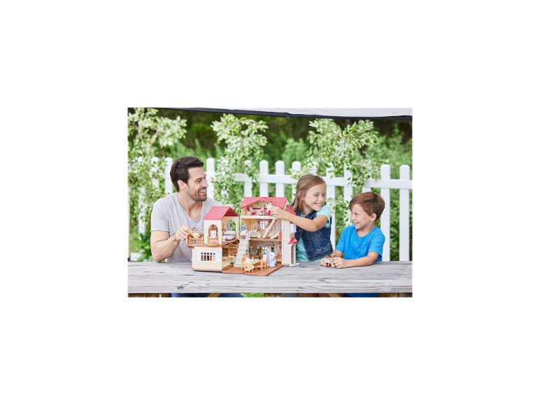 Vader en twee kinderen spelen met een groot poppenhuis op een houten tafel buiten.