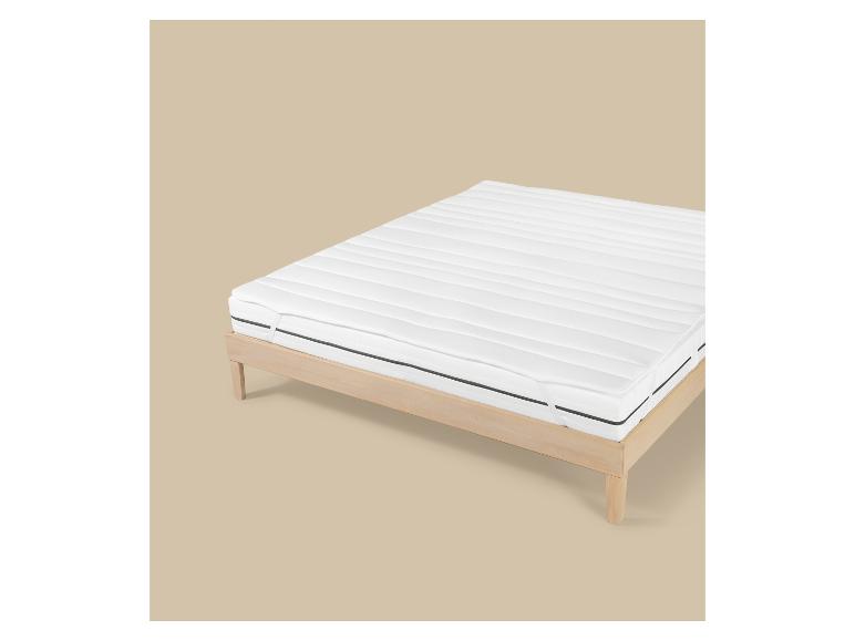 Houten bedframe met een wit matras en topper, op een beige achtergrond.