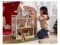 Een jong meisje speelt met een groot, meerverdiepings houten poppenhuis en accessoires.