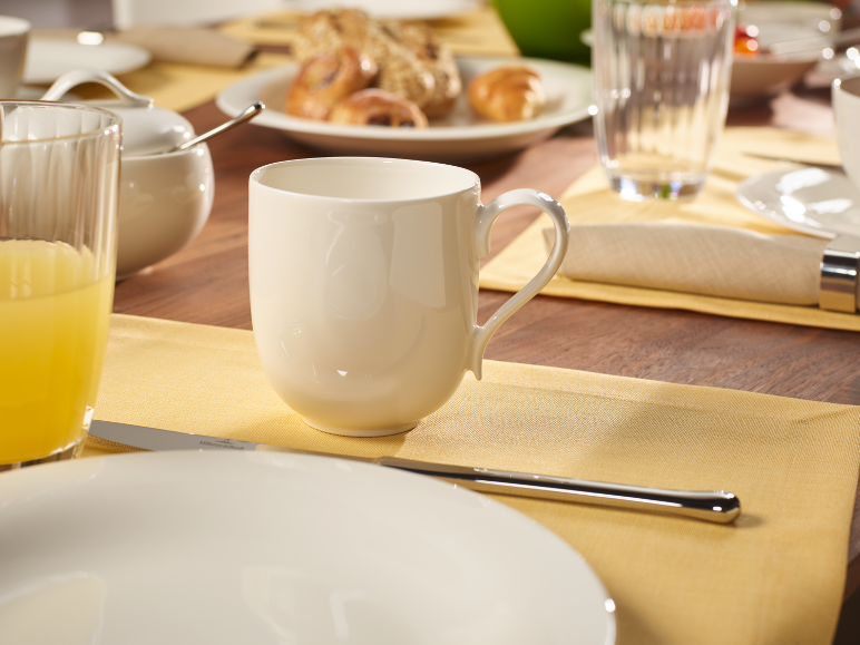 Ontbijttafel met een witte mok, sinaasappelsap en gebak op een houten tafel.