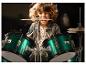 Een lachend kind speelt op een metallic groen drumstel.