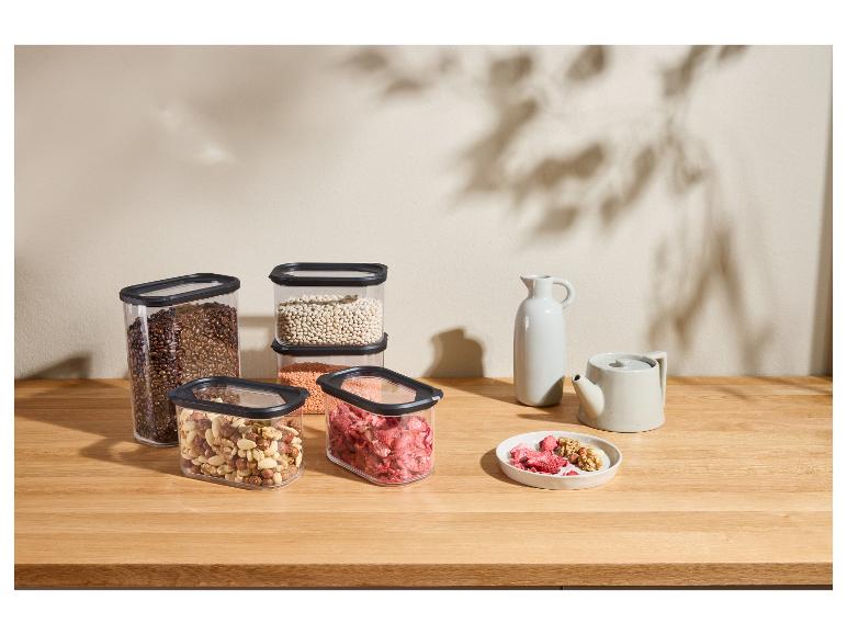 Transparante voedselcontainers met koffiebonen, noten, linzen en gedroogd fruit op een houten tafel.