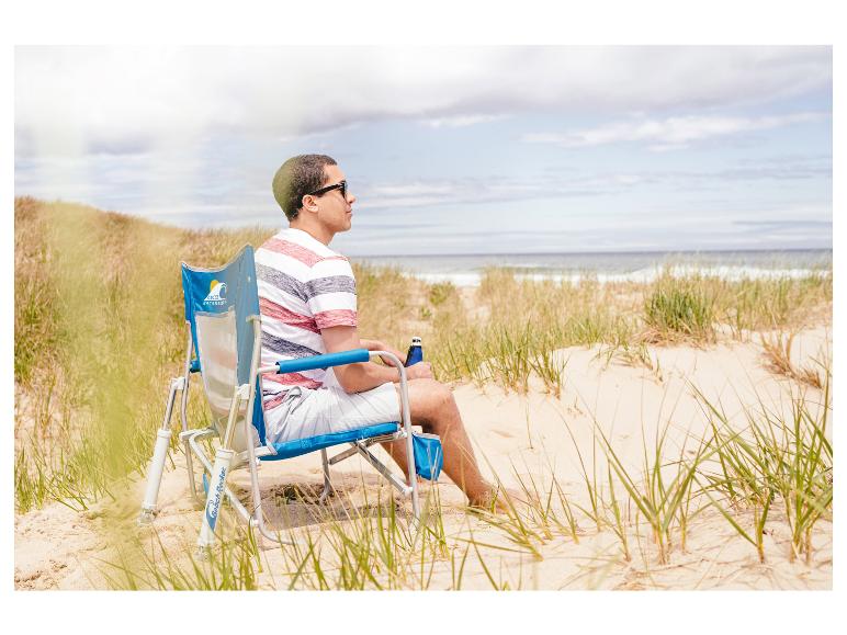 Een man die op een GCI-strandstoel op het strand zit.