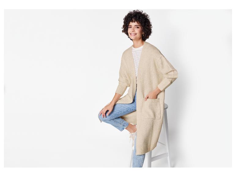 Een vrouw draagt ​​een beige gebreide cardigan en blauwe jeans.