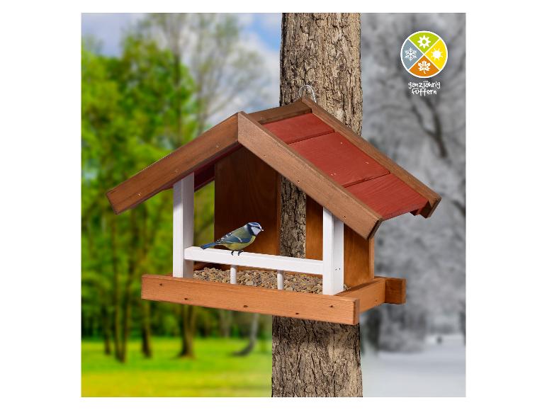 Houten vogelhuisje met een vogel aan een boom, met een gesplitste zomer- en winterachtergrond.