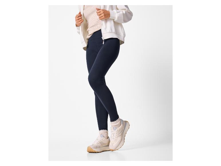 Vrouw in wit jack, beige top, marineblauwe legging en beige sneakers met ruchesokken.