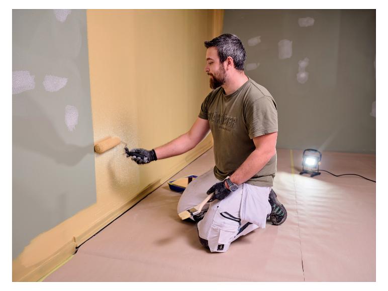 Man schildert muur, verlicht door LIVARNO® werklicht »The Painter«.