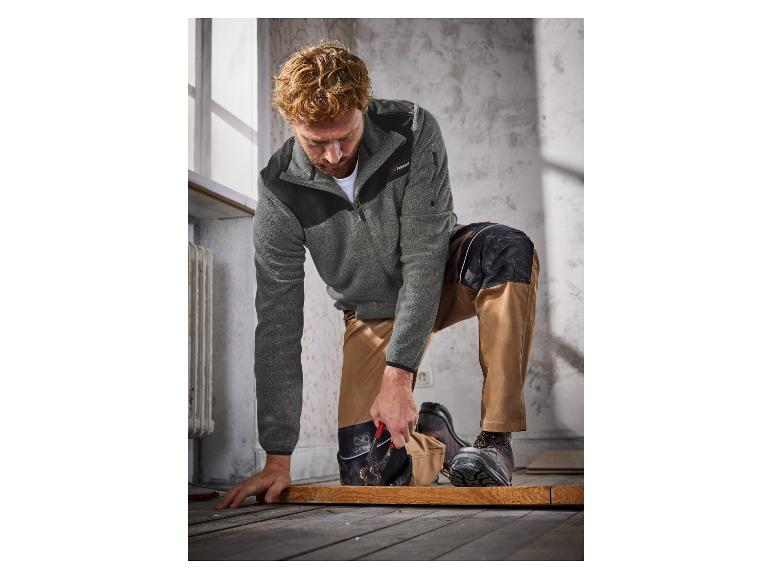 Een man in een grijze Parkside fleece trui en bruine werkkleding met kniebescherming, werkt met gereedschap.