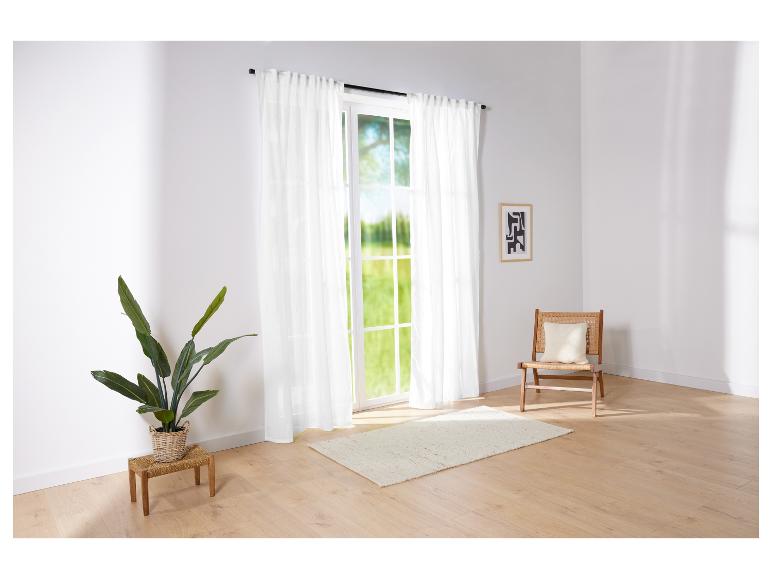 Lange witte gordijnen en een rotan stoel in een lichte kamer.